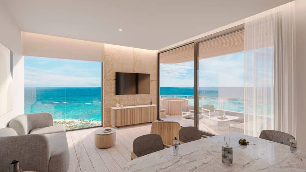 Interior view of a beachfront condo in Bao A, Puerto Morelos, showing a living area with large windows overlooking the ocean and a balcony with outdoor seating.