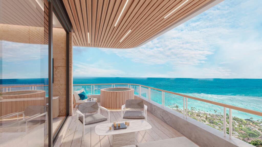 A spacious beachfront condo at BAO A in Puerto Morelos features a large balcony with outdoor seating and ocean views, with a hot tub and palm trees visible in the distance.