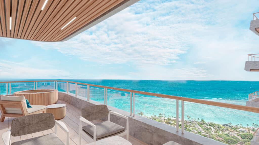 A spacious beachfront balcony at BAO B in Puerto Morelos features wooden accents, modern seating, and a stunning ocean view with a partly cloudy sky above.
