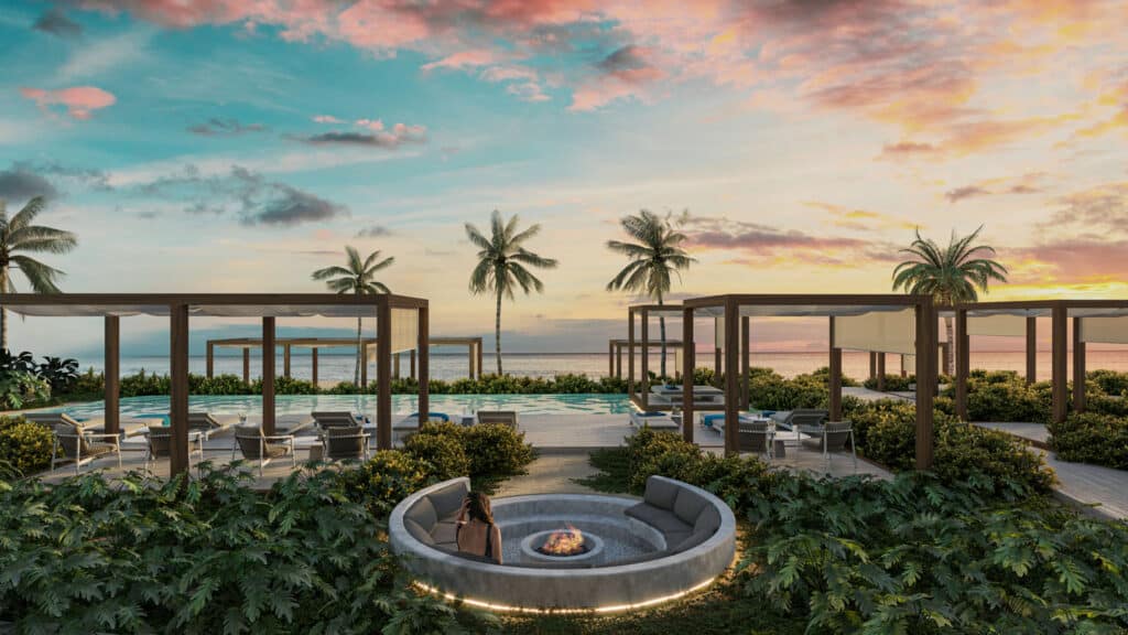 View of the Bao A beachfront condominium complex in Puerto Morelos with a hot tub, lounge chairs, palm trees, and a colorful sunset sky.