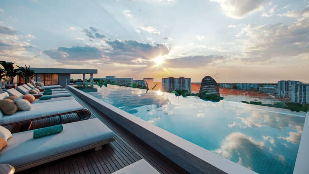 A luxurious rooftop pool at BLAS 1401 in Cancun's Marina Front area offers a relaxing space with sun loungers and a stunning view of the city skyline and sunset.