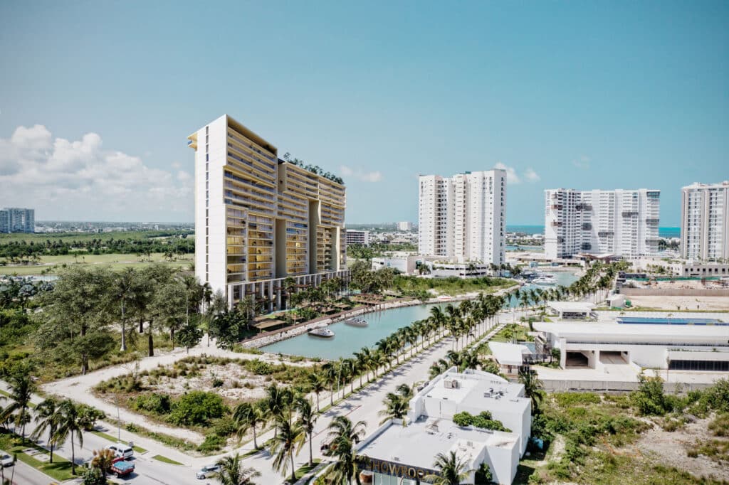 A modern residential building at BLAS 1401 in Cancun's Marina Front area, overlooking a canal with palm trees and adjacent high-rise buildings, under a bright blue sky.