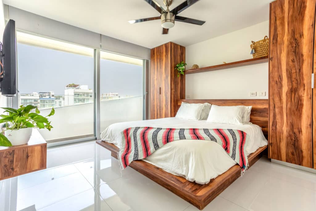 Modern bedroom with wooden accents and large window in DK05 – 401, Playa del Carmen, located in the Luis Donaldo Colosio area.
