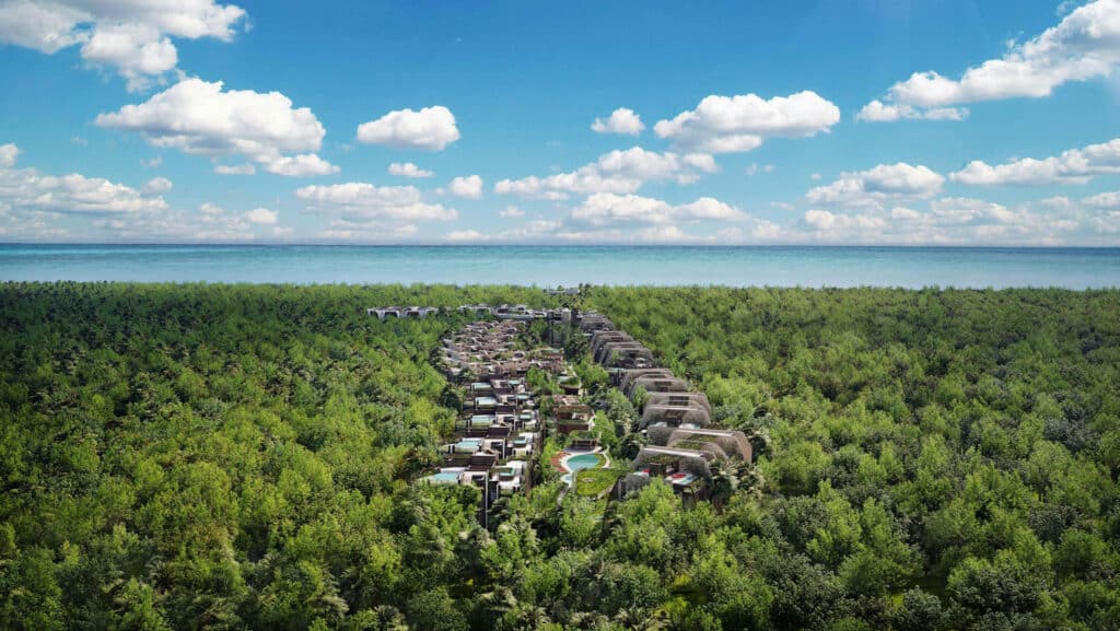Aerial view of Faena District B in Tulum, showing modern residences nestled among lush greenery with the ocean in the background on a partly cloudy day.