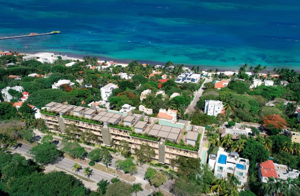 Aerial view of Soleii C in Playacar Phase 1, Playa del Carmen, showing a modern residential building with rooftop gardens surrounded by lush greenery, just steps from the coastline.