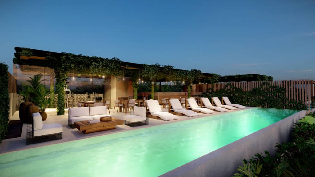 Outdoor pool area at Soleii C in Playacar Phase 1, Playa del Carmen, featuring lounge chairs, a shaded seating area, greenery, and soft lighting at dusk.