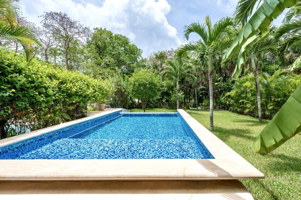 A private swimming pool surrounded by lush tropical trees and plants at Villa Victoria in Puerto Aventuras, near the Golf Course.