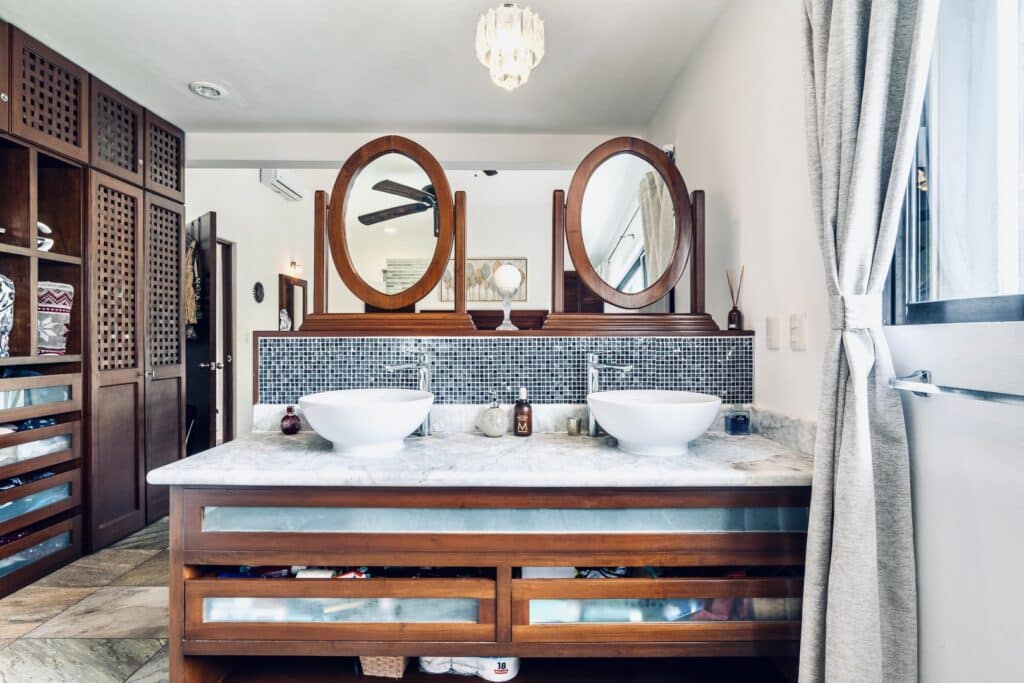 Bathroom with dual vessel sinks, wooden accents, mirror, and a view of the golf course at Villa Victoria in Puerto Aventuras.