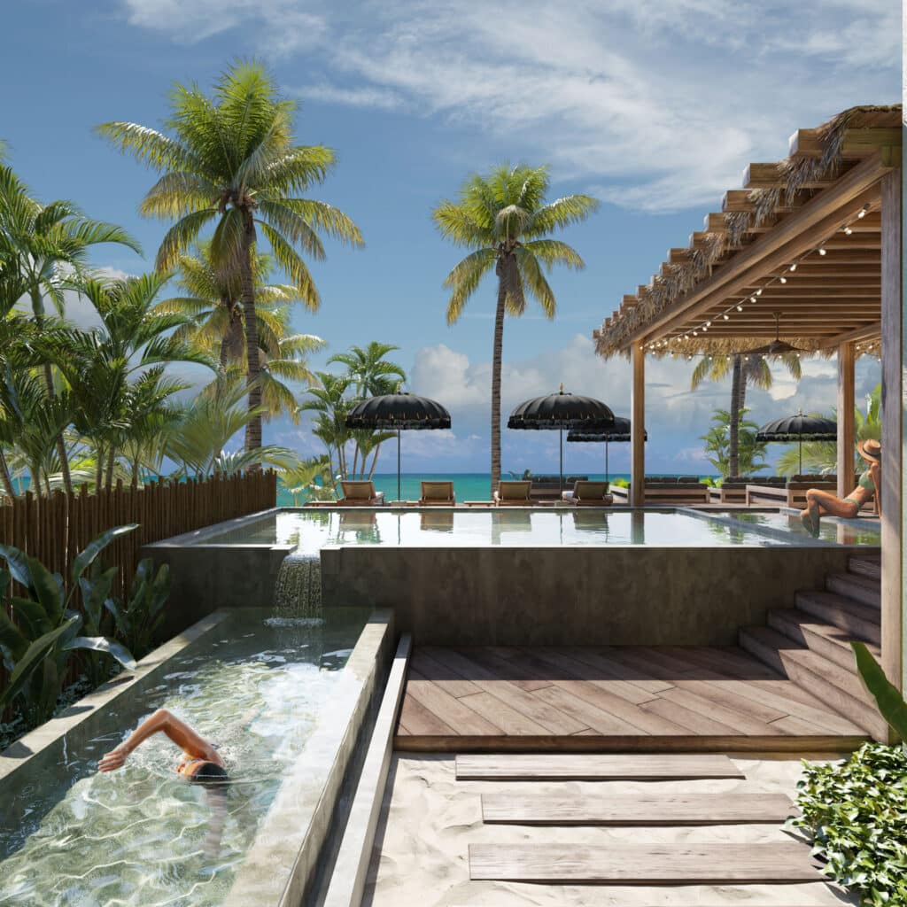 A view of Acalai 303 in Tulum showing a pool with a person swimming, surrounded by palm trees, lounge chairs with umbrellas, and overlooking the beachfront with a clear blue sky.