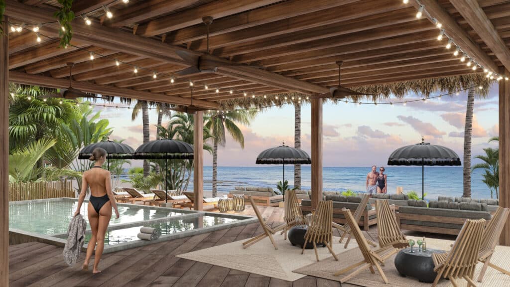 A woman in a black swimsuit walks past an outdoor hot tub under a wooden pergola with string lights, overlooking the beachfront in Tulum at Acalai 303 development.