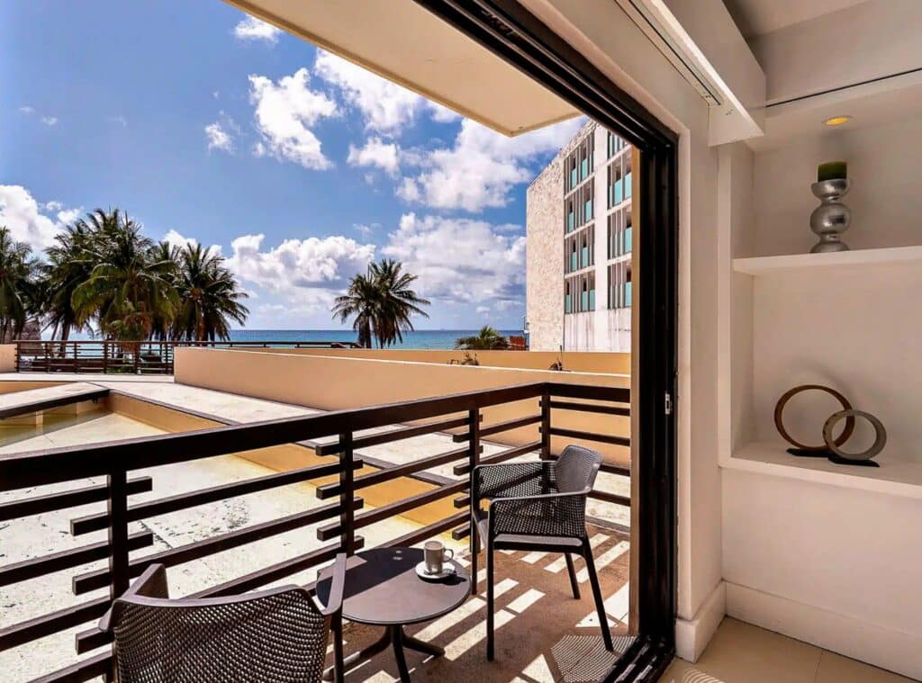 View of a balcony with palm trees, the ocean, and a partly cloudy sky in Playa del Carmen from an apartment at Aldea Thai.