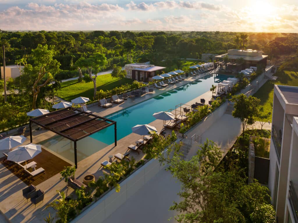 Aerial view of Banyan Tree Angsana A in Hacienda Xcanatun, Merida, showing a large swimming pool with lounge chairs, umbrellas, and lush surrounding greenery at sunset.