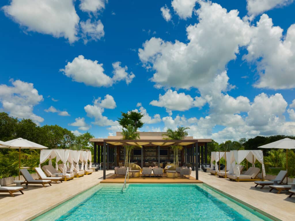 A luxurious penthouse at Banyan Tree Angsana A in Hacienda Xcanatun, Merida, with a view of a swimming pool and shaded lounge areas under a bright blue sky with fluffy clouds.