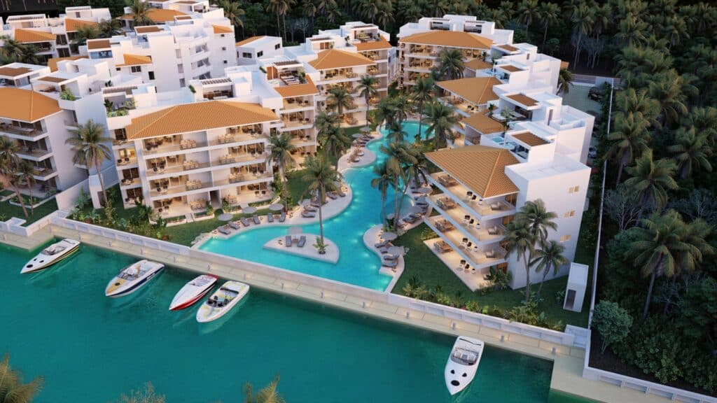 Aerial view of Marina Aqua A in Puerto Aventuras showing a marina-front development with white multi-story buildings, a winding pool surrounded by palm trees, and boats docked at the waterfront.