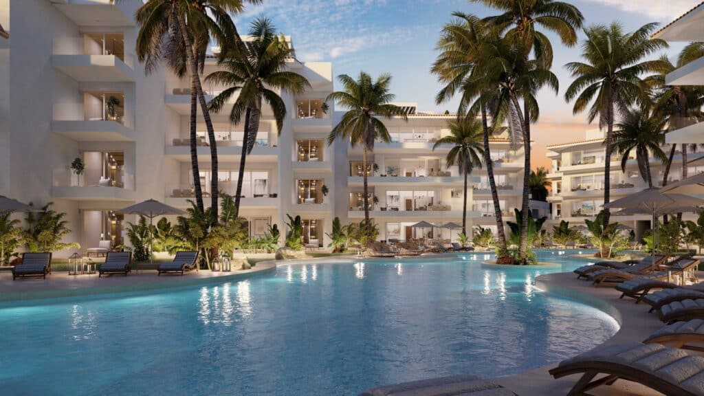 A modern apartment in Marina Aqua A with a spacious balcony overlooking the marina front, surrounded by palm trees and a large swimming pool at sunset in Puerto Aventuras.