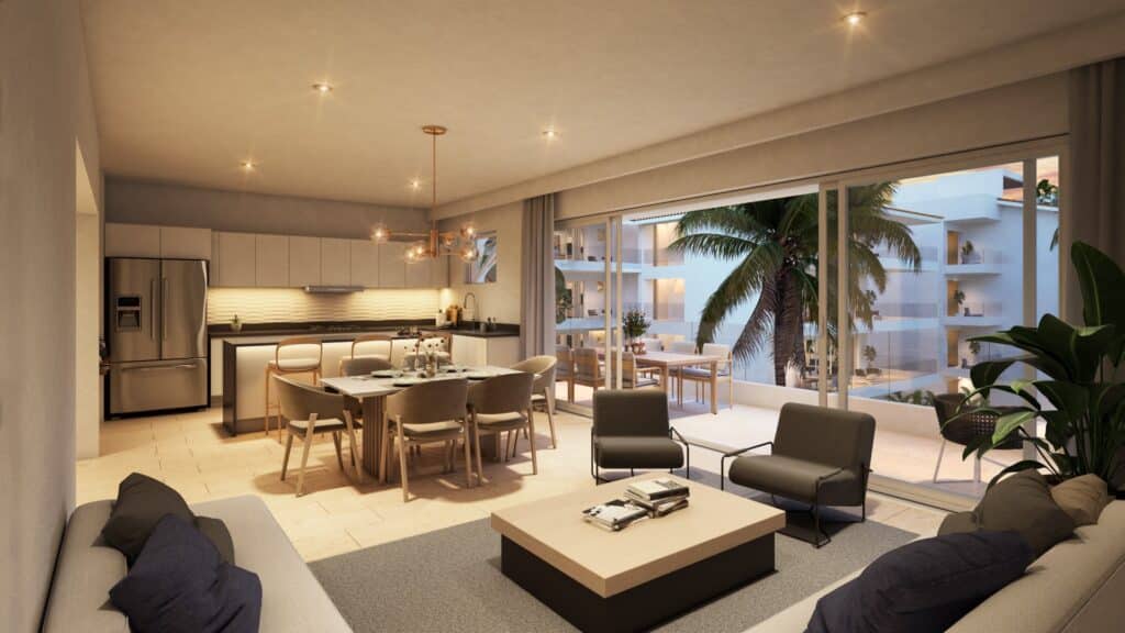 Interior view of a Marina Aqua A apartment in Puerto Aventuras, showcasing an open living area with a dining space, modern kitchen, and a balcony with a view of a palm tree and neighboring buildings.