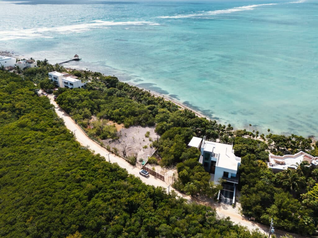 Aerial view of Tankah Bay Beachfront Land in Tulum, featuring lush greenery, a sandy coastline, and modern buildings along the shoreline.