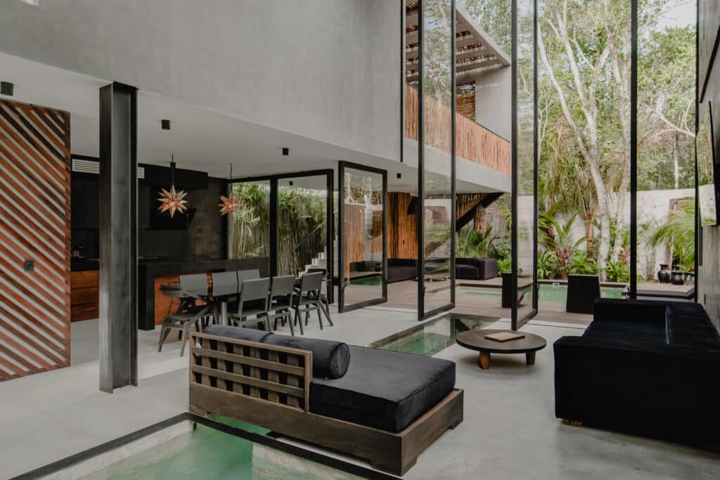 Interior view of Villa Niburu in Tulum, featuring a spacious living area with large glass windows, modern furnishings, and a glimpse of the outdoor garden and pool area.