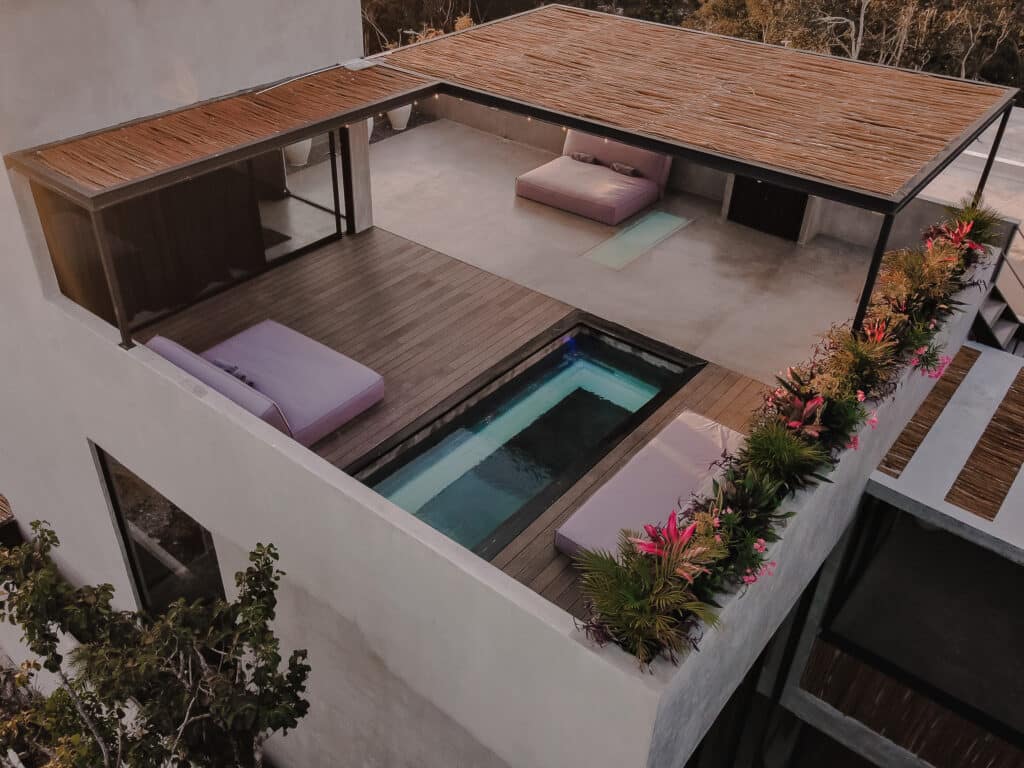 Aerial view of Villa Niburu in Tulum, featuring a rooftop terrace with a small pool, wooden deck areas, outdoor seating, and decorative plants along the edge.