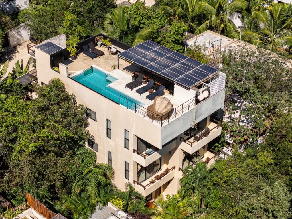 Aerial view of a 10-unit boutique hotel in La Veleta, Tulum, featuring a rooftop pool, lounge chairs, solar panels, and lush surrounding greenery. — 10 Unit Hotel/Apartment.