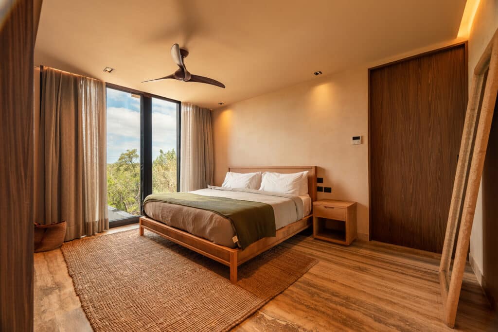 Bedroom in a property at Bespoke D9 in Tulum's Tankah Bay with wooden furniture, large windows, natural light, and neutral decor.