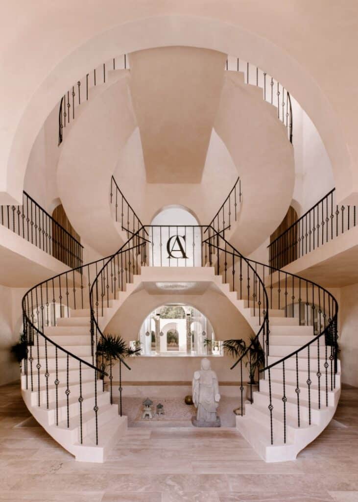 Interior view of Casa Arka in Tulum, featuring a striking double staircase with black wrought iron railings, a central statue, and arched architectural details in Region 15.