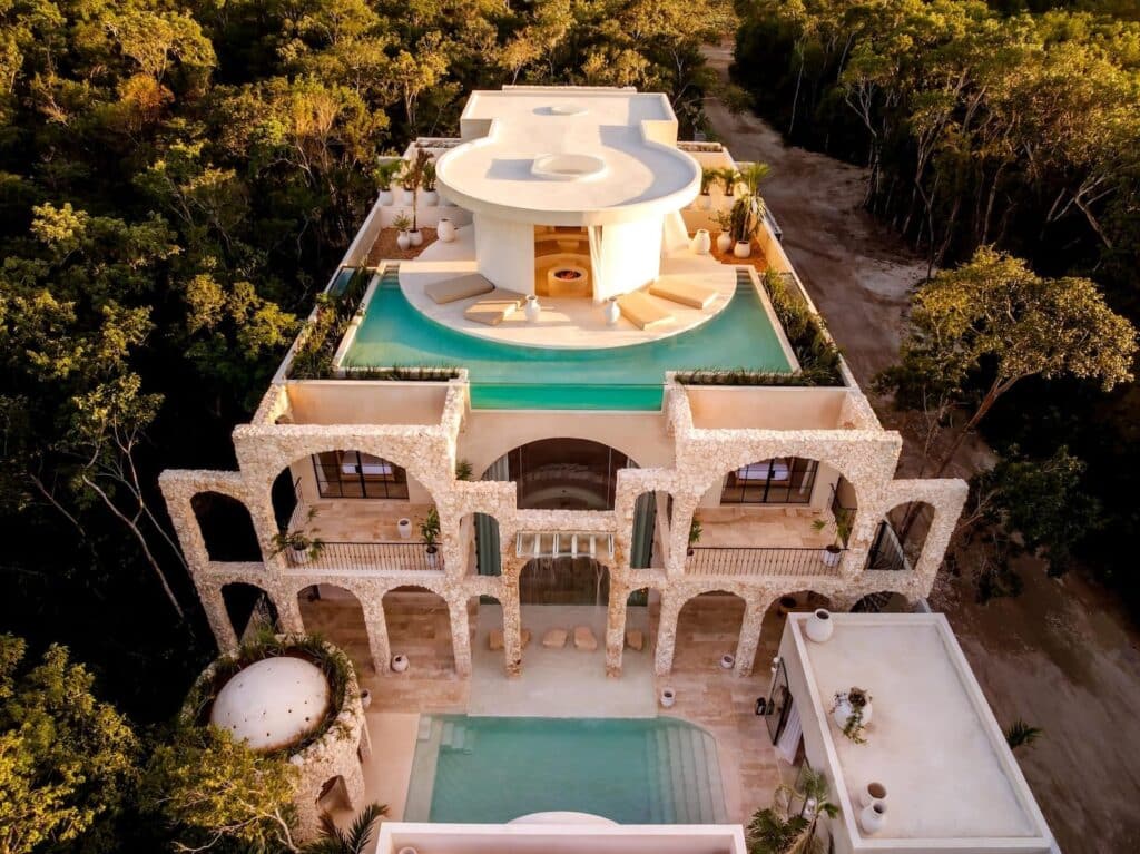 Aerial view of Casa Arka in Tulum's Region 15, showcasing a modern multi-level house with a swimming pool surrounded by lush greenery and stylish outdoor seating areas.