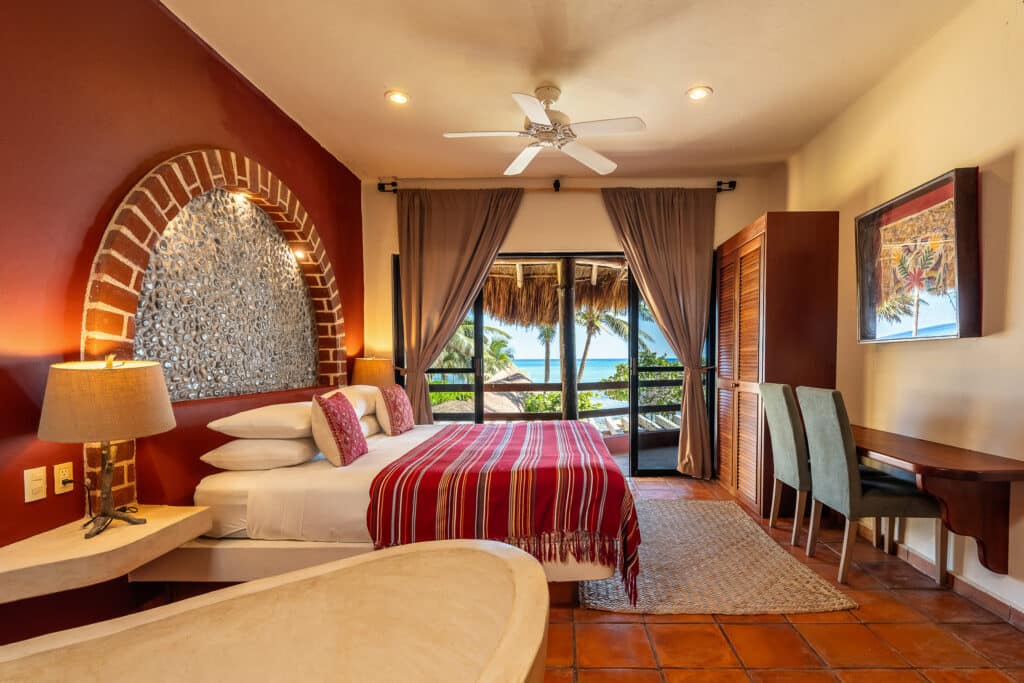Interior of Casa Zen Del Sol at Jade Bay 8 in Akumal, showcasing a bedroom with a balcony overlooking beachfront views, tropical decor, and warm lighting.