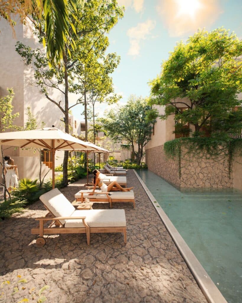 A serene outdoor pool area at Qanaai Nah 101 in Santa Ana, Merida, with lounge chairs, umbrellas, lush trees, and clear water under a sunny sky.
