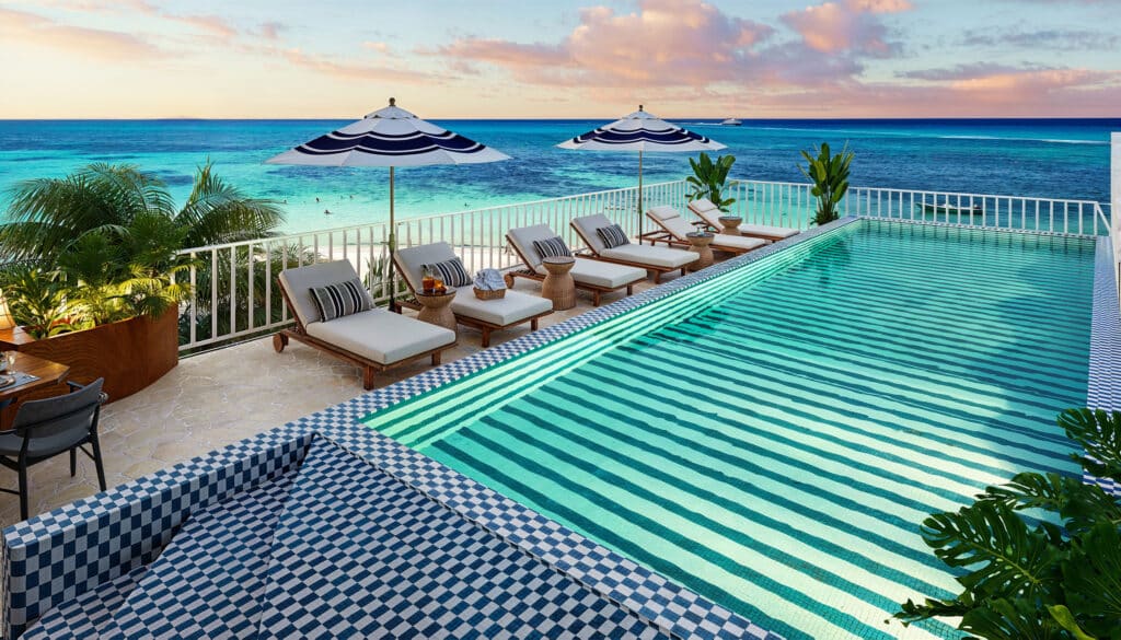 View from Saint Marine 305 in Playa del Carmen showing a beachfront infinity pool, lounge chairs with umbrellas, and the ocean beyond at sunset.