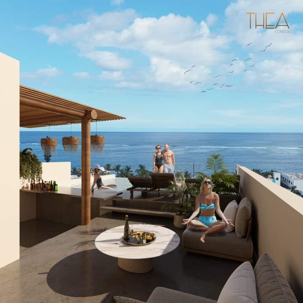 A view from Thea 502 in Puerto Morelos showing a rooftop lounge area with people relaxing and enjoying the ocean breeze, overlooking the Caribbean Sea with a partly cloudy sky.