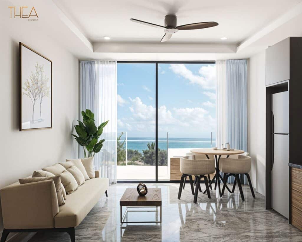 A modern living room in Thea 502, Puerto Morelos, featuring a large window with ocean views, a cream sofa, a wooden coffee table, and a dining area with four chairs.