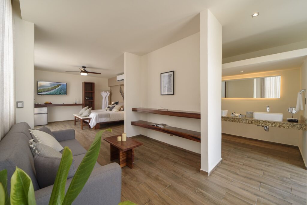 Interior view of the 25 Room Boutique Hotel in Aldea Zama, Tulum, showing a spacious living area with a sofa, a bedroom with a large bed, and a modern bathroom.