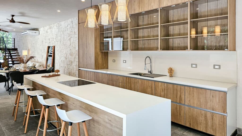 Modern open-concept kitchen inside Villa Coral in Aldea Zama, Tulum, featuring wooden cabinets, a white island with barstools, and minimalist decor.