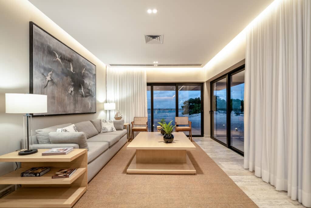 Interior view of Bonanza PH-1214 in Marina Front, Progreso, featuring a living room with a beige sofa, wooden furniture, white curtains, and large sliding glass doors.