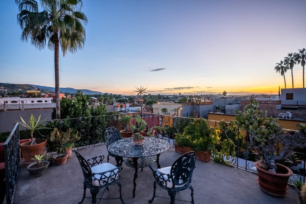 View of a terrace with potted plants and wrought-iron furniture overlooking San Miguel de Allende's Centro Histórico at sunset.