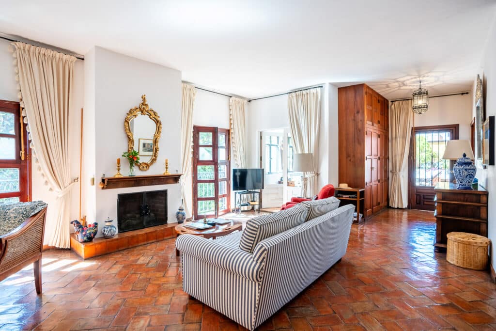 Living room in Casa Carolina in the Centro Histórico area of San Miguel de Allende, featuring terracotta tile floors, wood accents, and large windows with curtains.