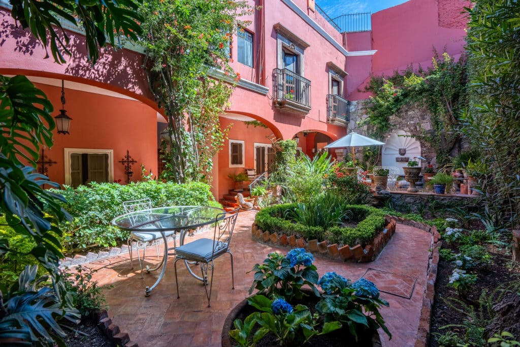 Courtyard of Casa Carolina in San Miguel de Allende's Centro Histórico features vibrant pink walls, lush greenery, outdoor seating, and decorative details.