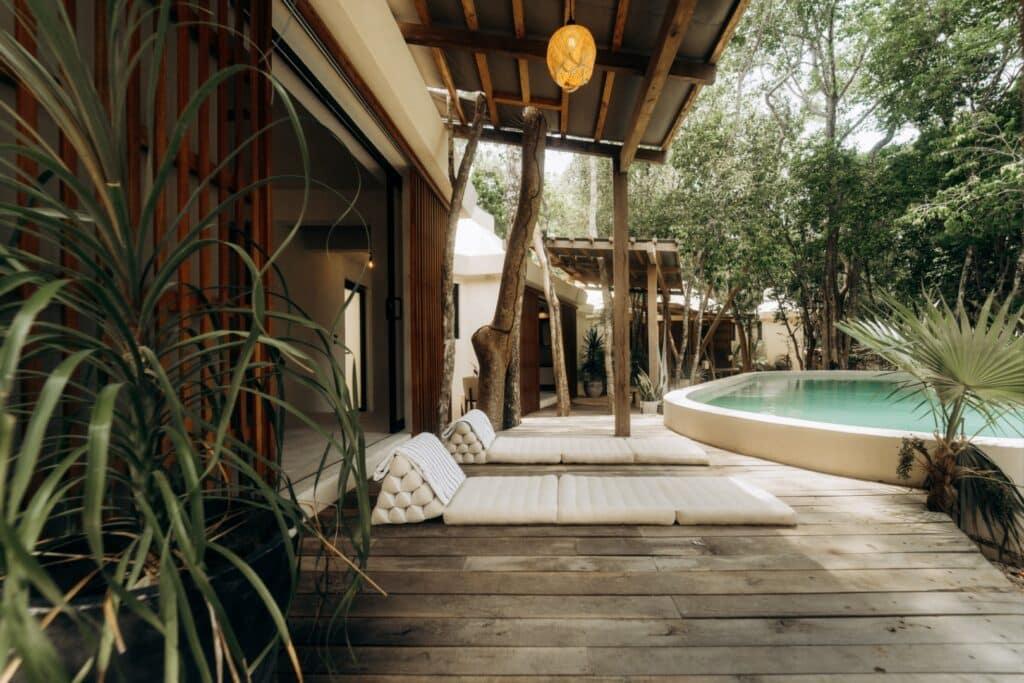 A wooden deck area at Casa Oox in Tulum features a small swimming pool, sun loungers, and surrounding lush green trees, creating a peaceful outdoor retreat.