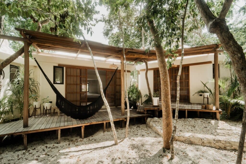 A cozy house with a wooden deck kitchen area in Casa Oox development, surrounded by trees and lush plants in Tulum's Region 15.