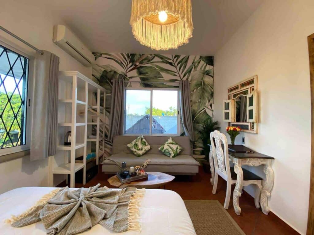 Interior of the Castillo 5 at Centro Tulum 6 Room Hotel in Tulum, featuring a cozy seating area with a sofa, decorative pillows, tropical-themed wallpaper, and stylish furniture.