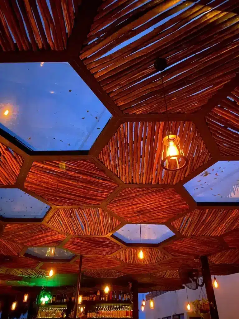 Interior view of Maka rooftop bar at Centro Tulum, featuring a wooden slat ceiling with hexagonal skylights and warm hanging lights.