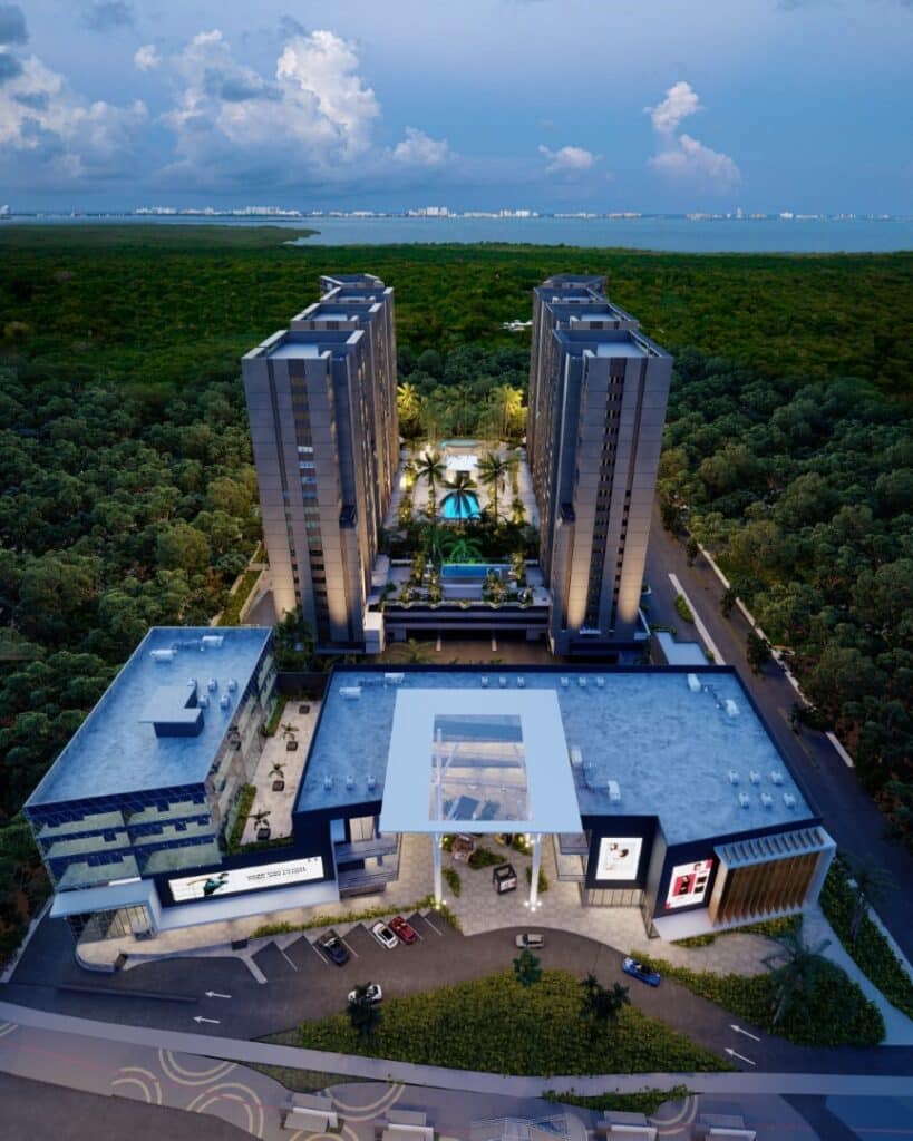 An aerial view of Manglar Cumbres L-402 in Cancun, showing modern high-rise buildings surrounded by lush greenery, with a pool and recreational area in the central courtyard.
