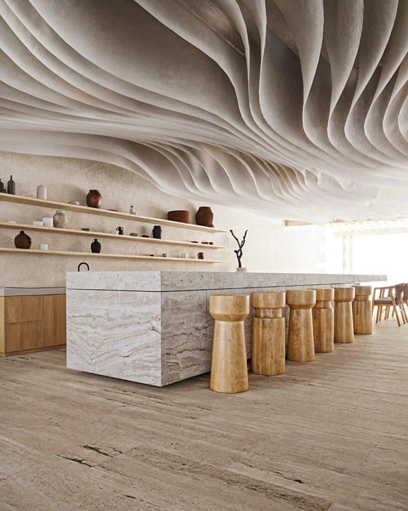 A modern interior with a marble kitchen island, wooden stools, and minimalist shelves on a textured wall, inside the Maranta 203 Beachfront development in Tulum.