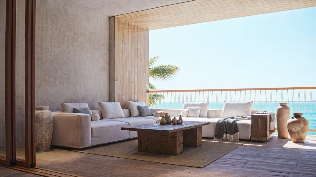 Living room with a beachfront view in Maranta 203 Beachfront, Tulum, featuring a large white sofa, wooden coffee table, and decorative vases overlooking the sea.