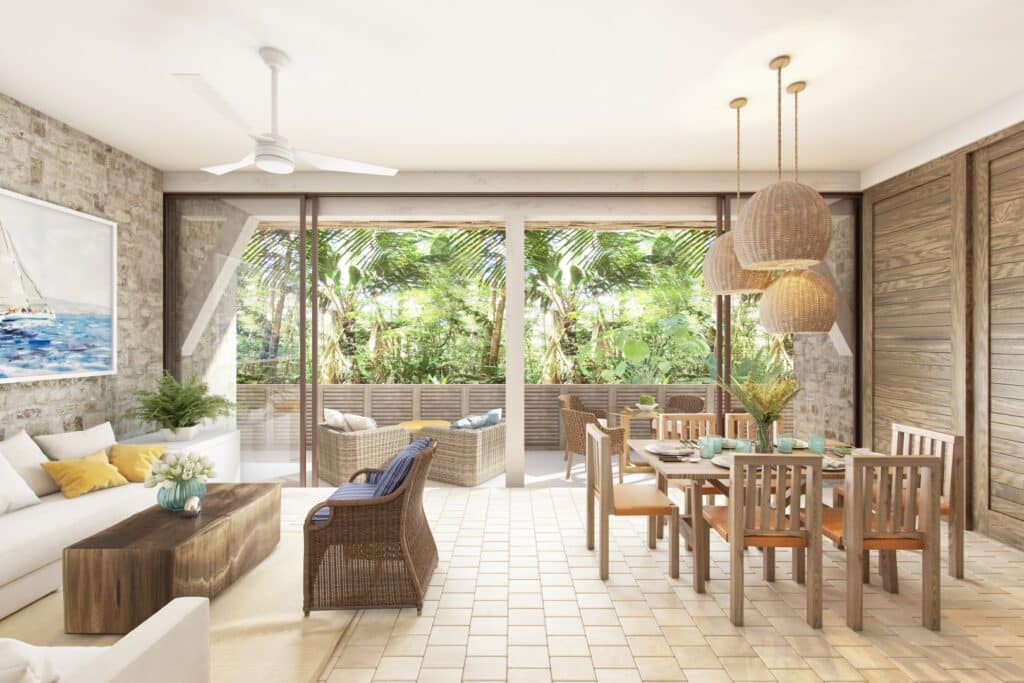 A bright living and dining area at Puerta Azul Tulum 101 in Aldea Zama, Tulum, featuring a woven pendant light, wicker furniture, and large glass doors opening to lush greenery.