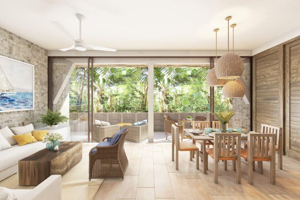 Interior view of a living and dining area at Puerta Azul Tulum 101 in Aldea Zama, Tulum, featuring a neutral color palette, wooden accents, wicker furniture, and large windows with lush greenery outside.