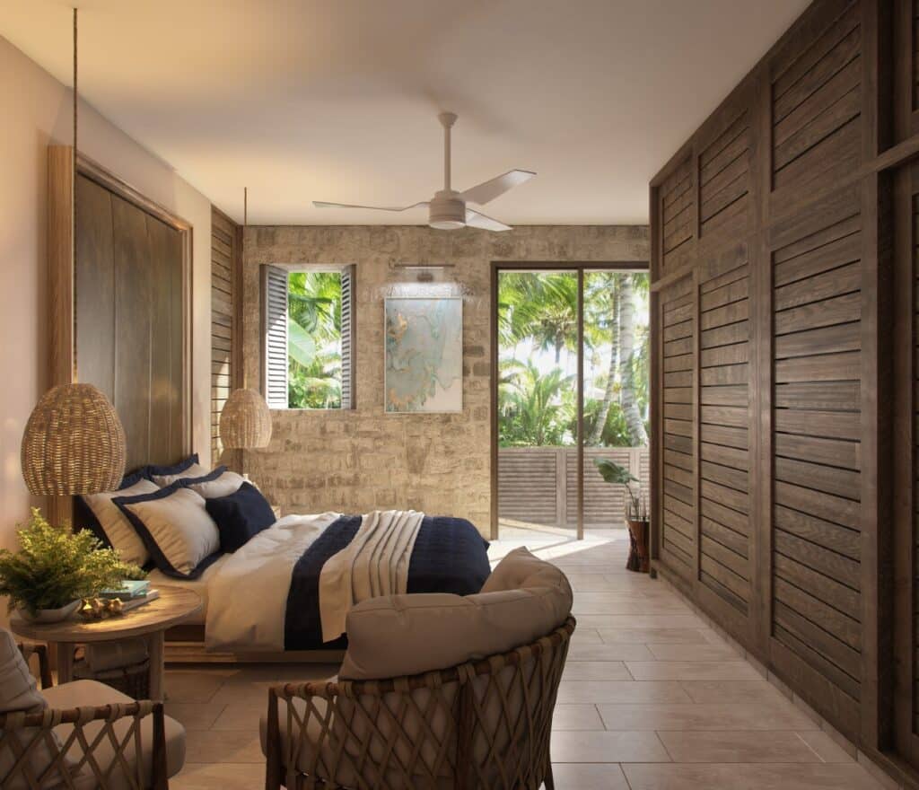 A cozy bedroom at Puerta Azul Tulum 101 in Aldea Zama, Tulum, featuring a stone wall, wooden accents, tropical views through large glass doors, and minimalist decor.
