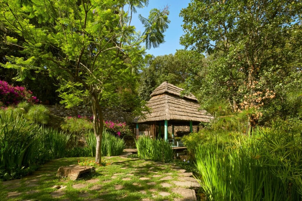 A thatched-roof gazebo surrounded by lush greenery and colorful flowering plants in Cerro Colorado at Ah0 Art Villa &., Loma De Rodriguez.