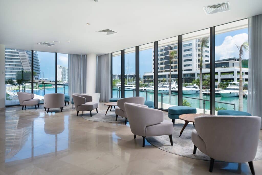 A spacious lounge area at Blume 1C in Puerto Cancun, features floor-to-ceiling windows offering views of yachts and modern high-rise buildings in the marina.